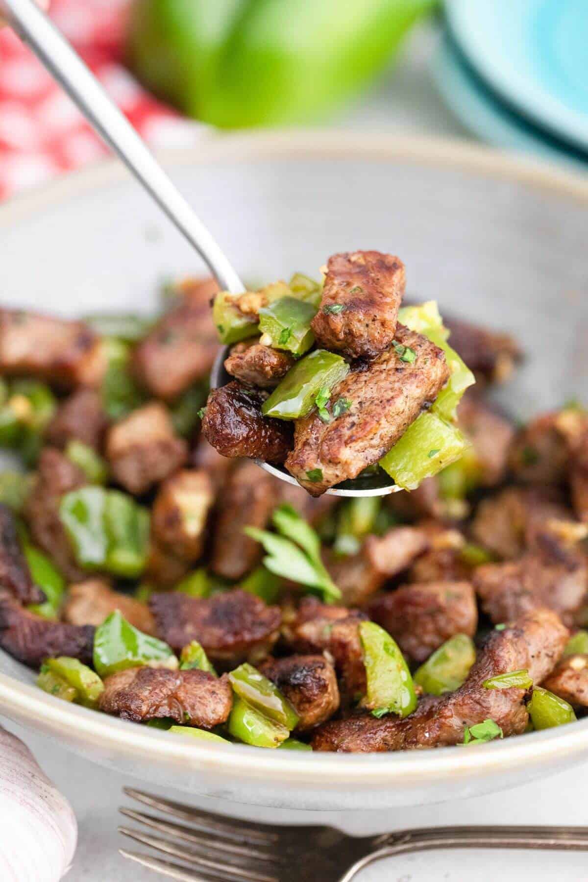 A bowl of garlic butter steak bites with green pepper with some on a spoon.