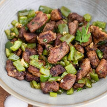 A bowl of meat and green peppers on a wooden table.