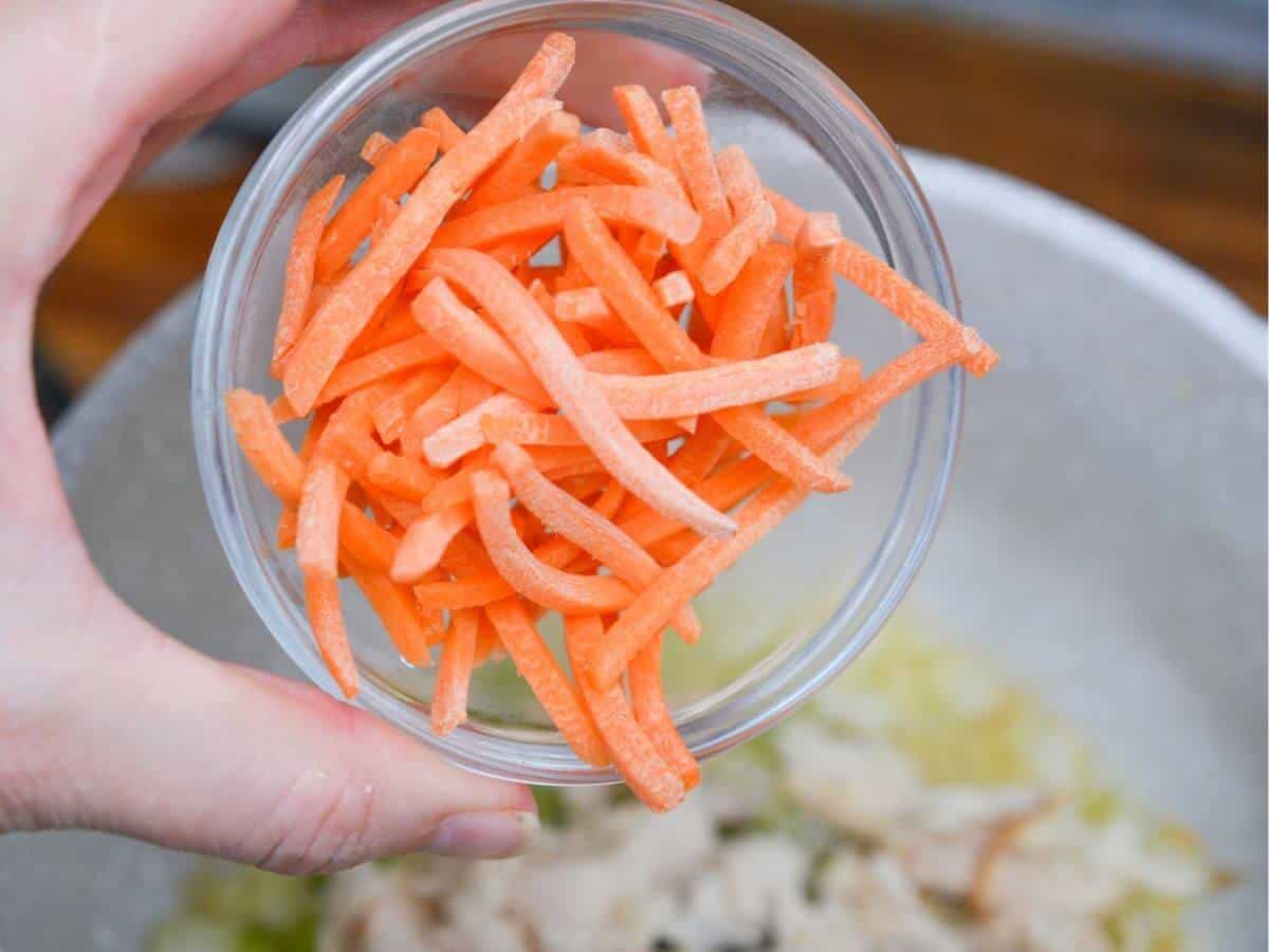 A person holding matchstick carrots in a bowl.