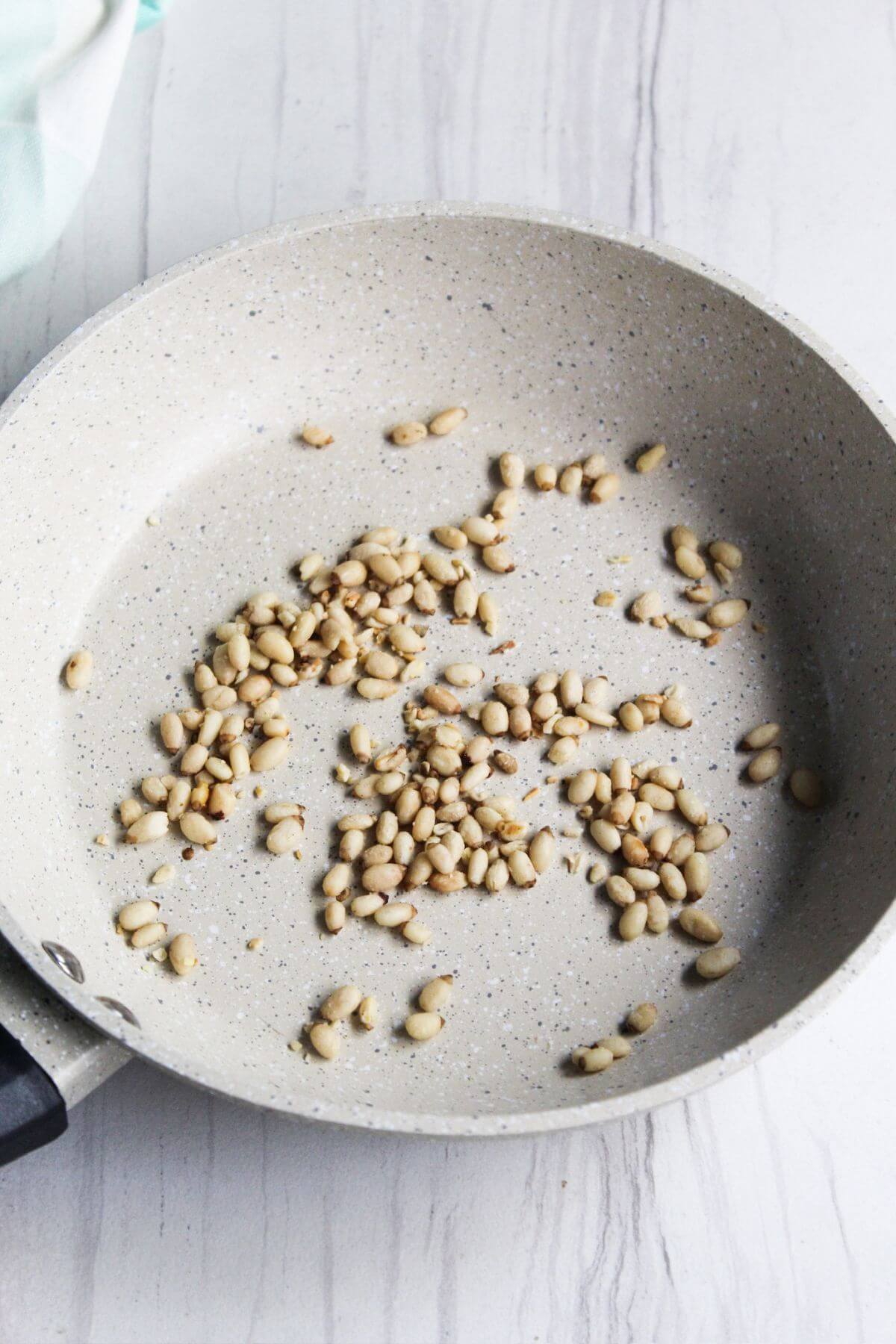 A frying pan with pine nuts in it.