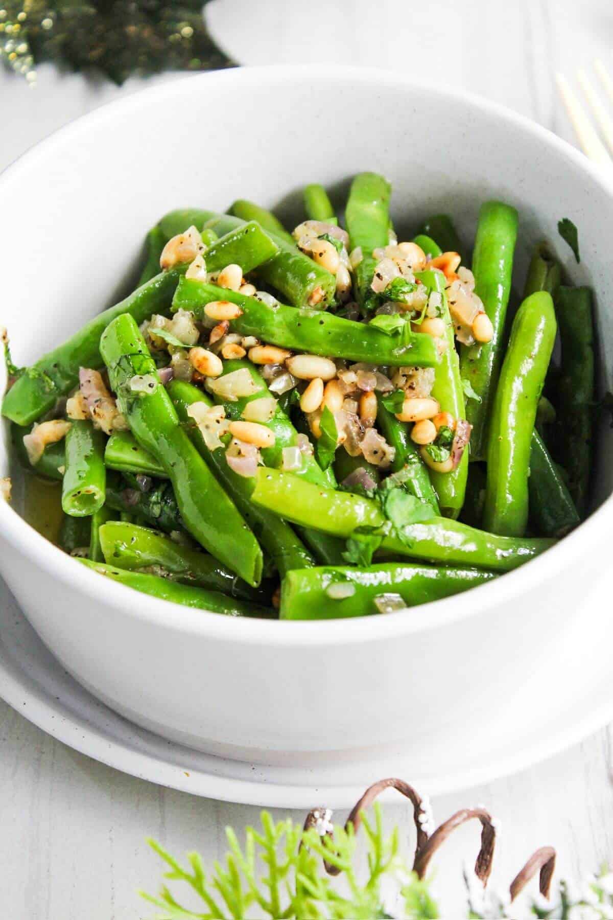 A white bowl with garlic butter green beans and pine nuts.