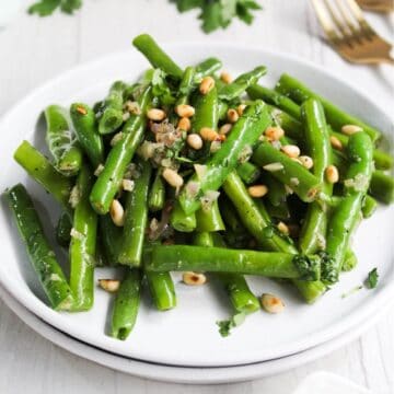 Green beans with pine nuts on a white plate.