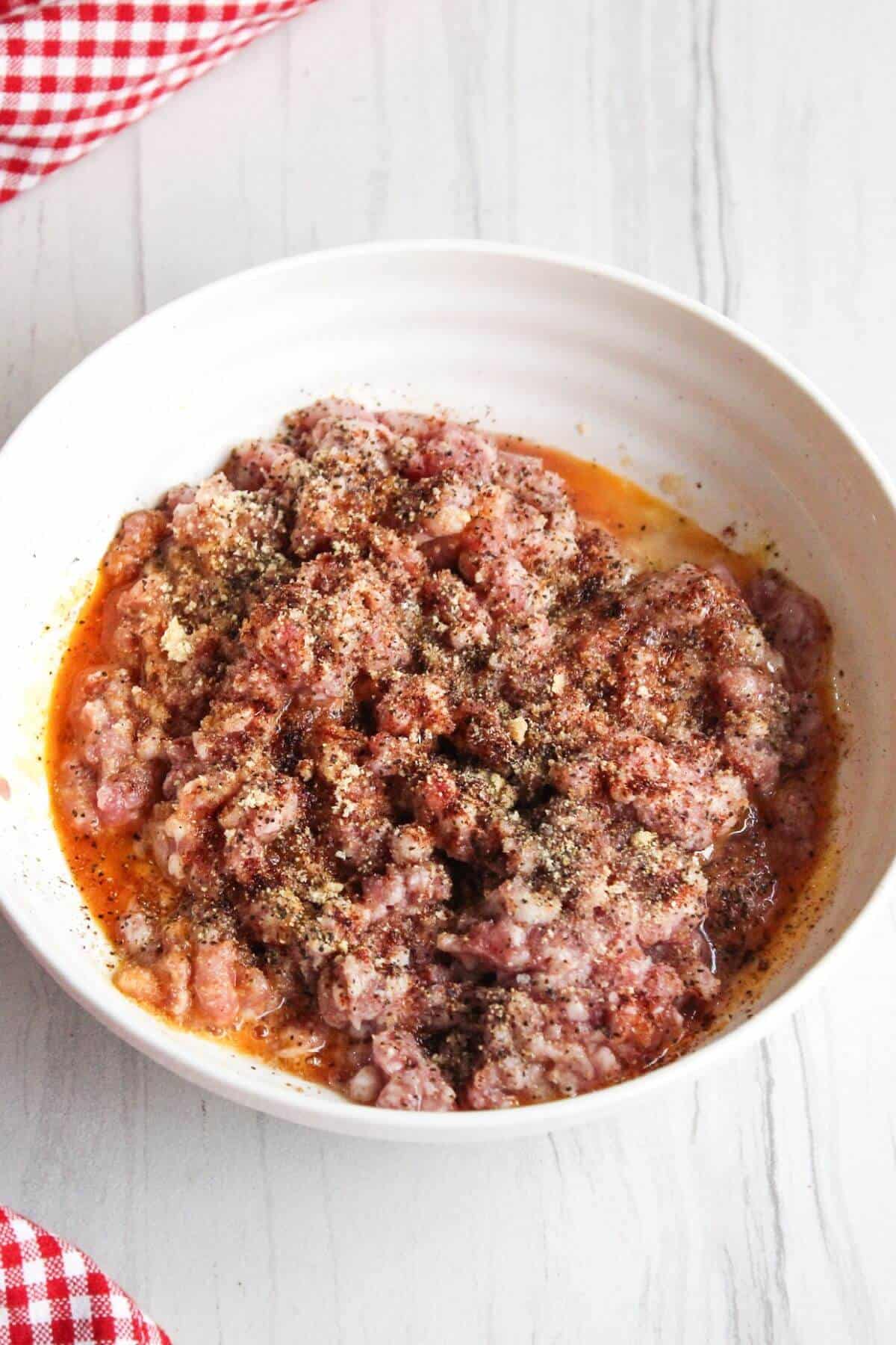A bowl of ground pork and seasonings in a white bowl.