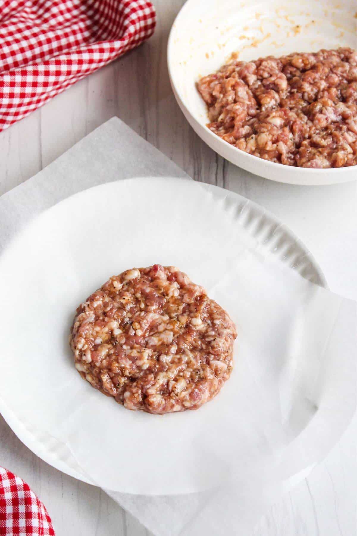 Ground pork patty on a plate with bowl of meat mixture in back.