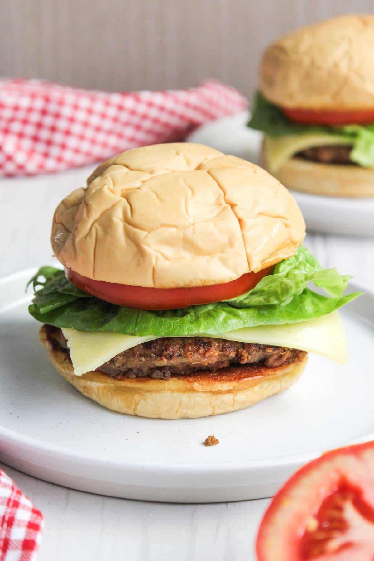 Two pork burgers on a plate with tomatoes and lettuce.
