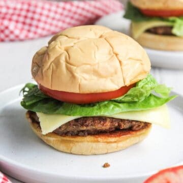Two burgers on a plate with lettuce and tomatoes.