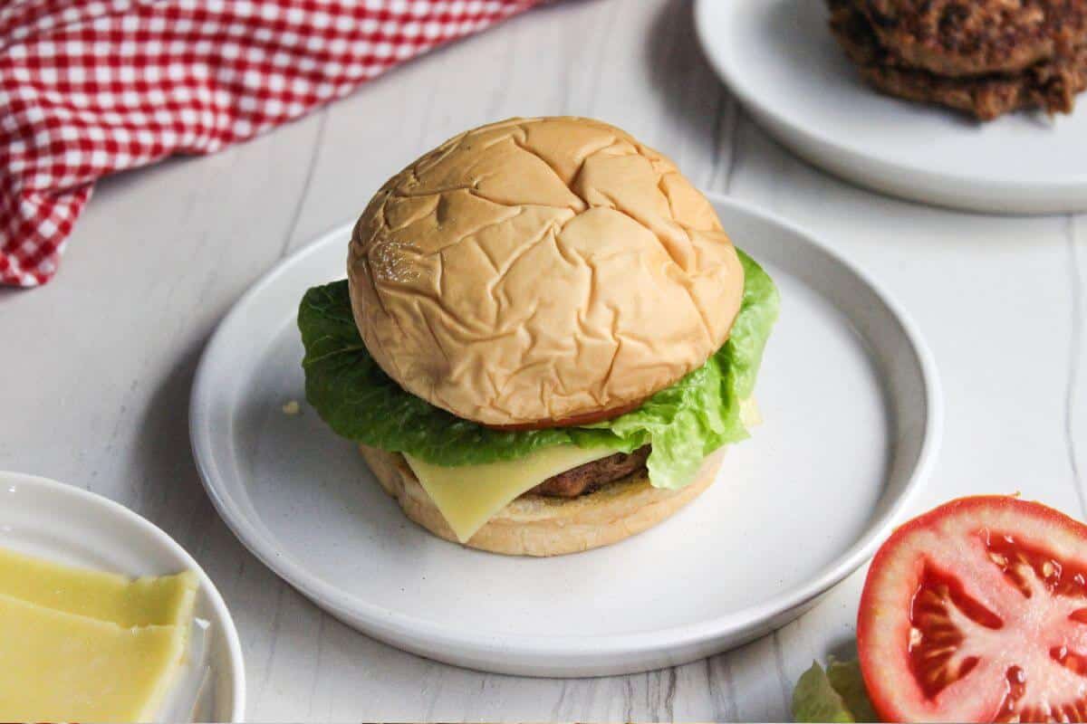 A plate of ground pork burgers with tomatoes, lettuce and cheese.