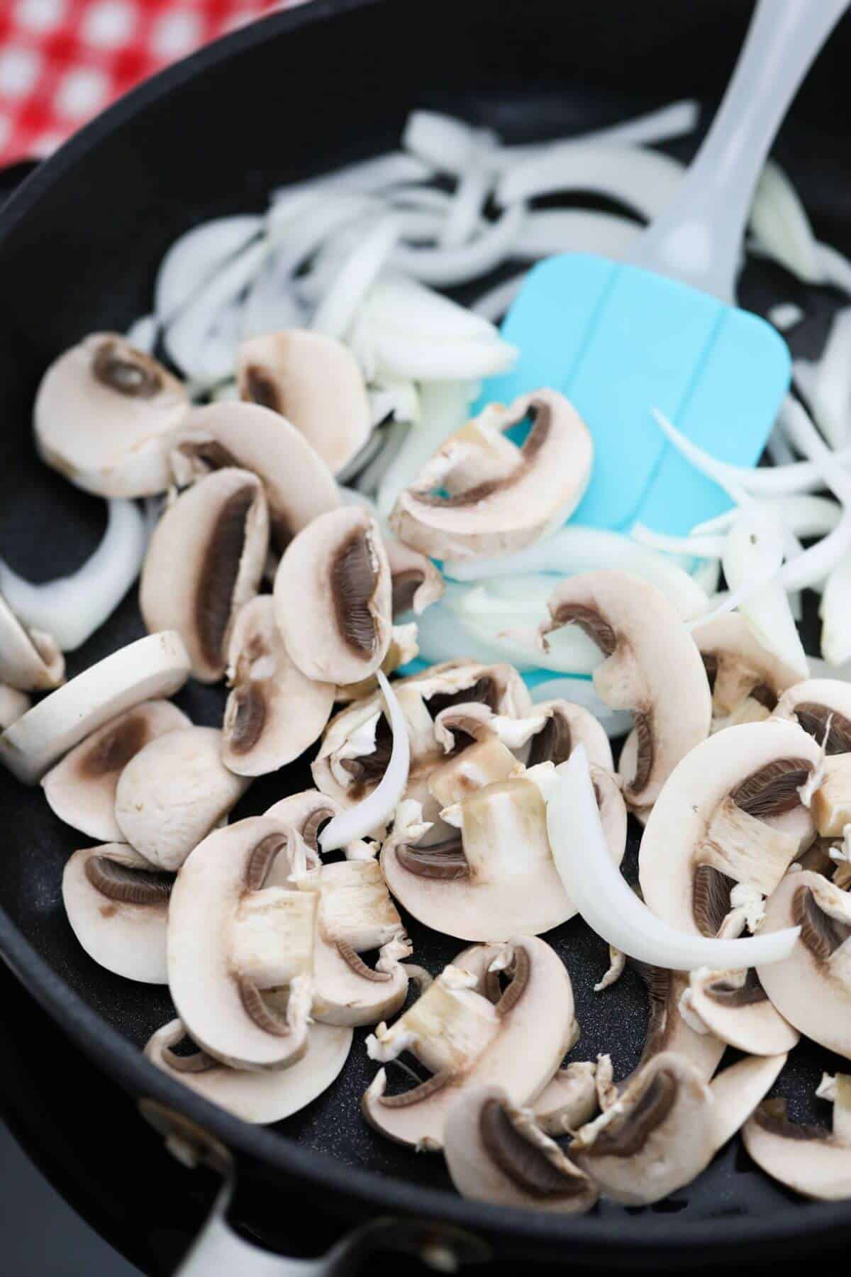 Mushrooms and onions in a pan with a blue spatula.