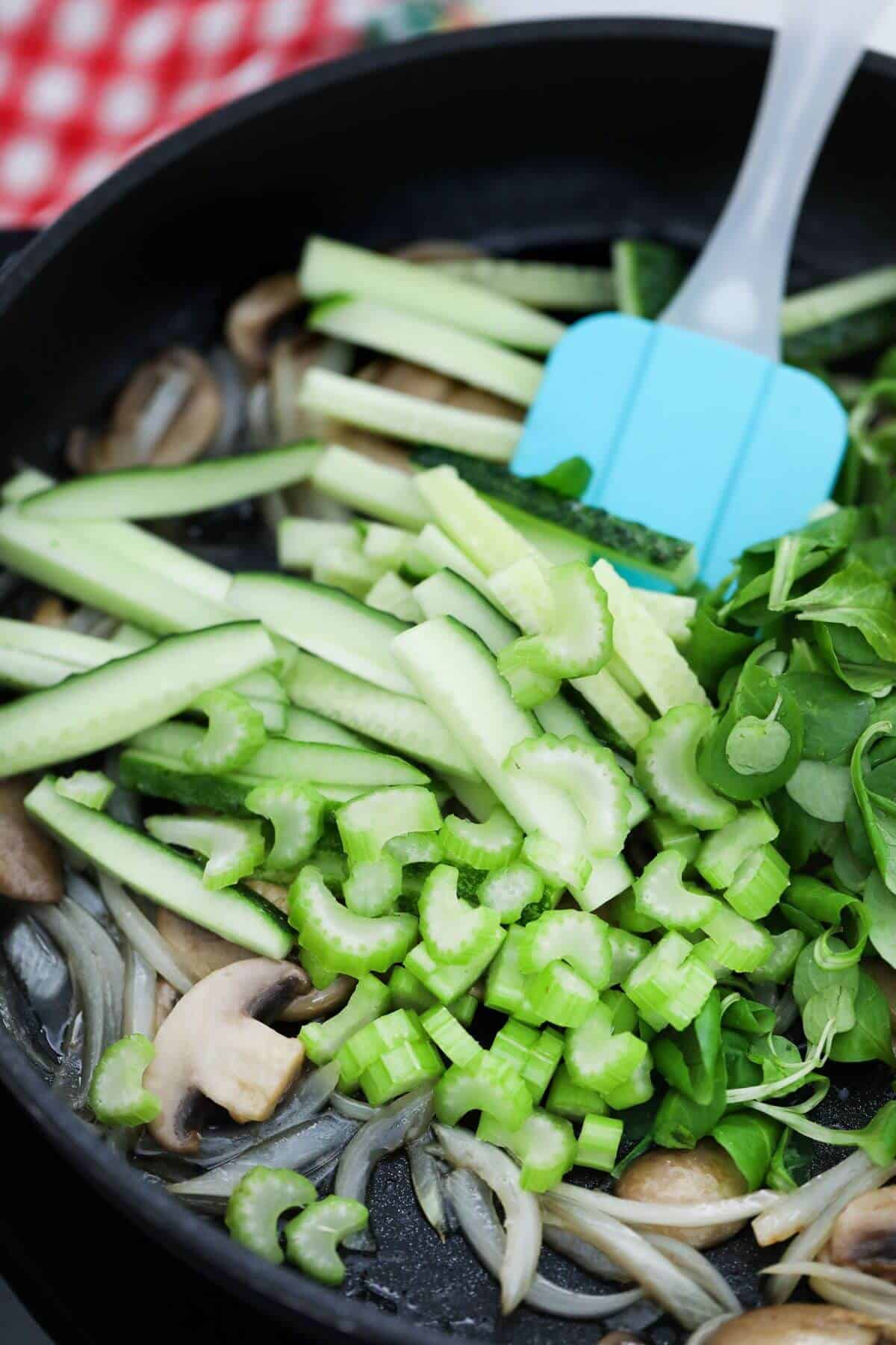 A frying pan filled with vegetables and a blue spatula.
