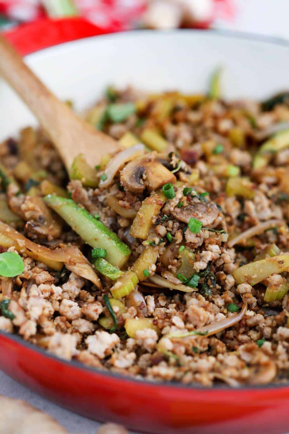Ground pork with vegetables in a pan with a wooden spoon.