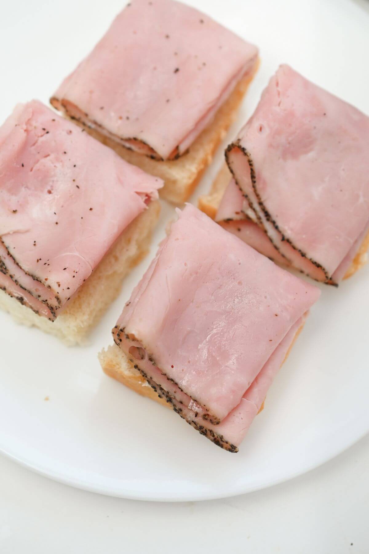 Four slices of ham on a white plate.