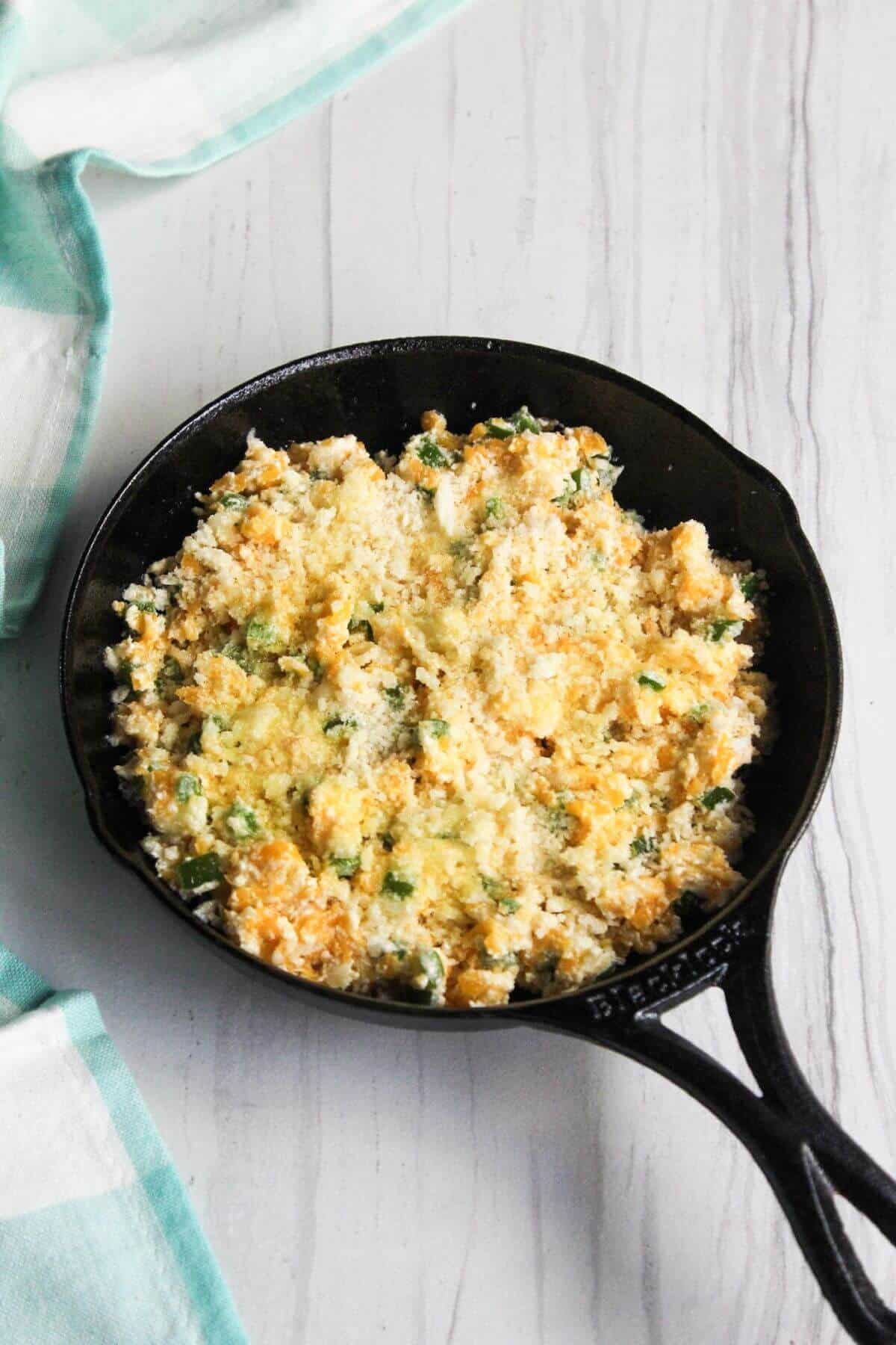 A cast iron skillet filled with jalapeño dip mixture topped with panko.