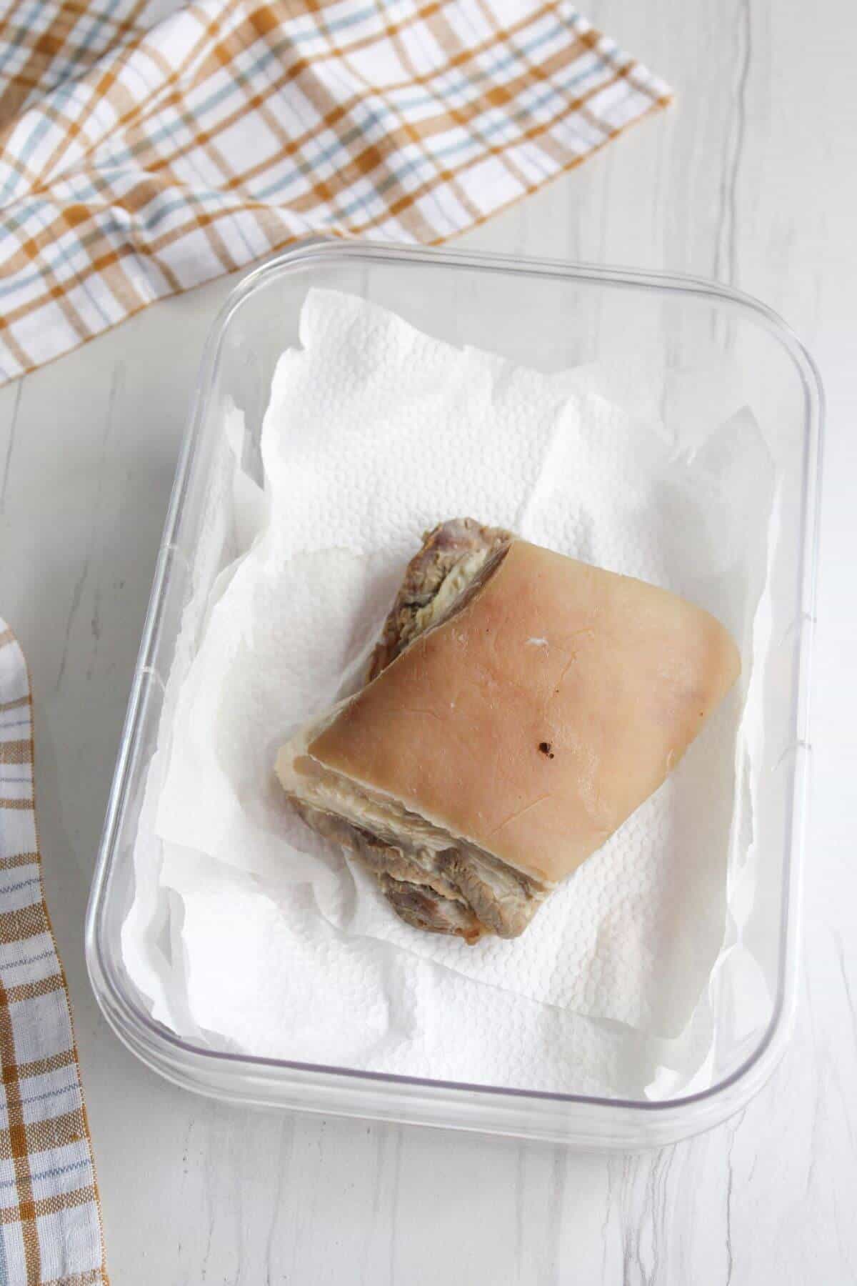 A piece of boiled pork belly in a container on top of a paper towl.