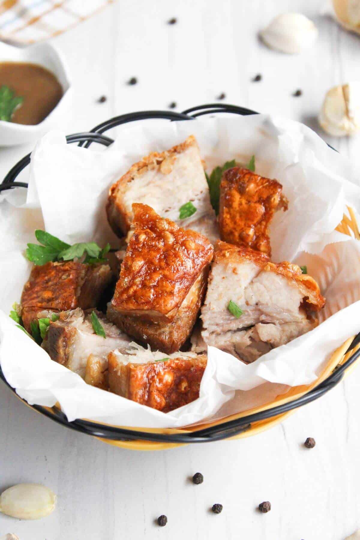 A bowl of lechon kawali with a sauce behind it.