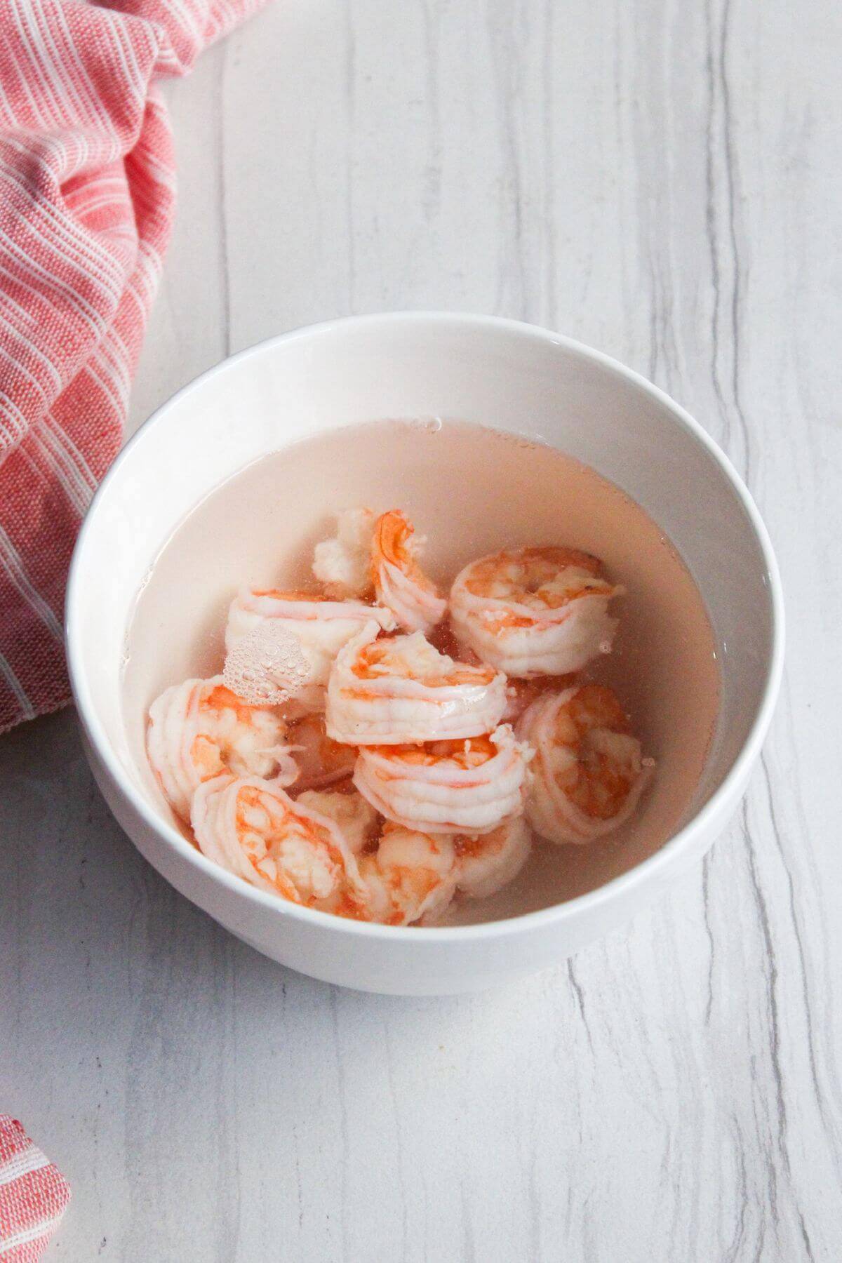 Shrimp in a white bowl with water next to a red towel.