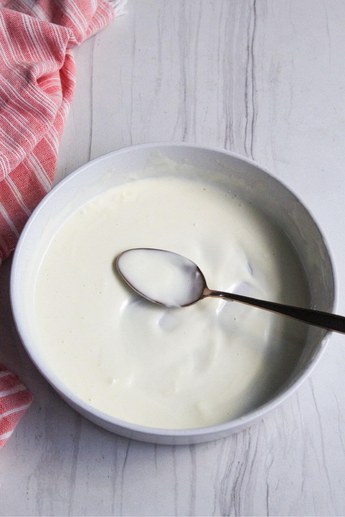 A bowl of mayonnaise based dressing with a spoon in it.
