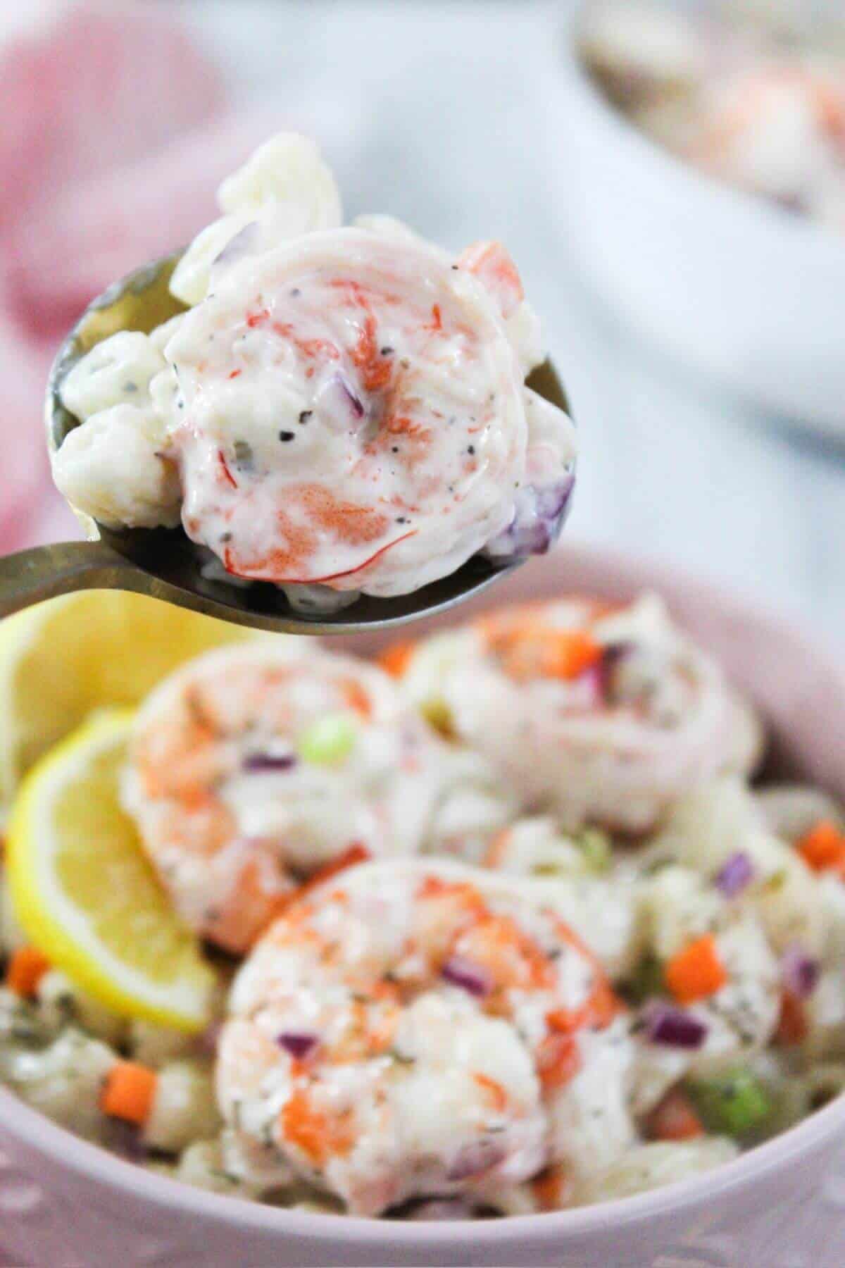 A spoonful of shrimp macaroni salad in a pink bowl.
