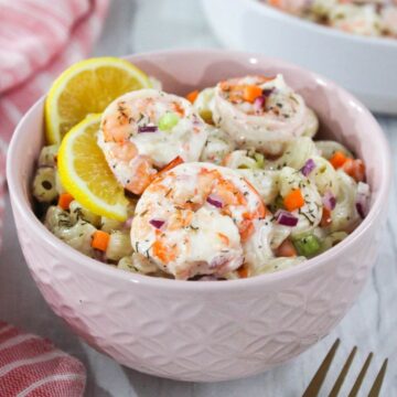Shrimp pasta salad in a pink bowl with lemon wedges.