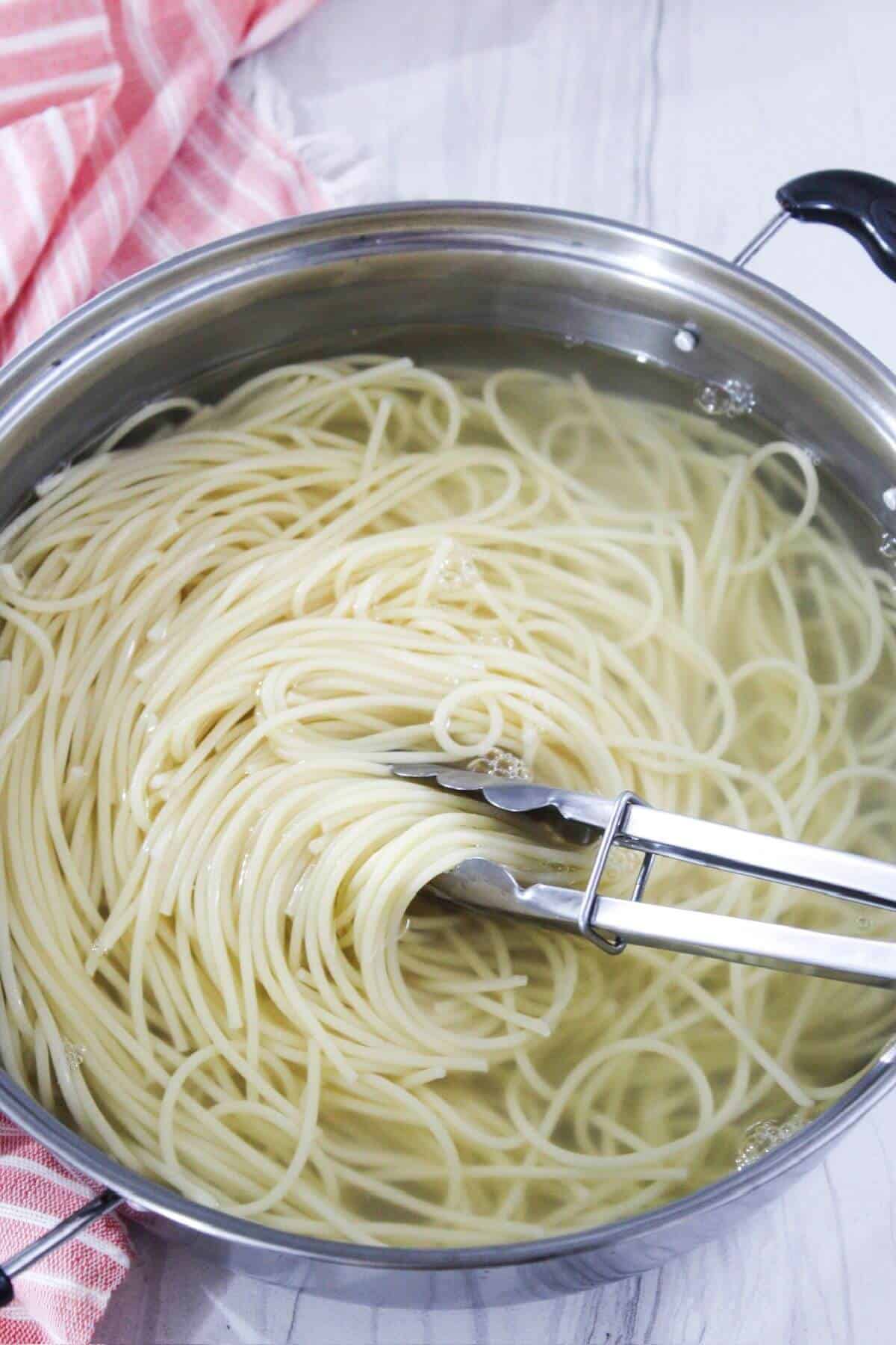 Spaghetti in a pan with two tongs.