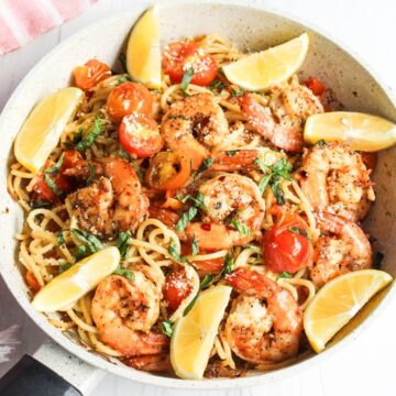 A skillet filled with shrimp, tomatoes and basil.