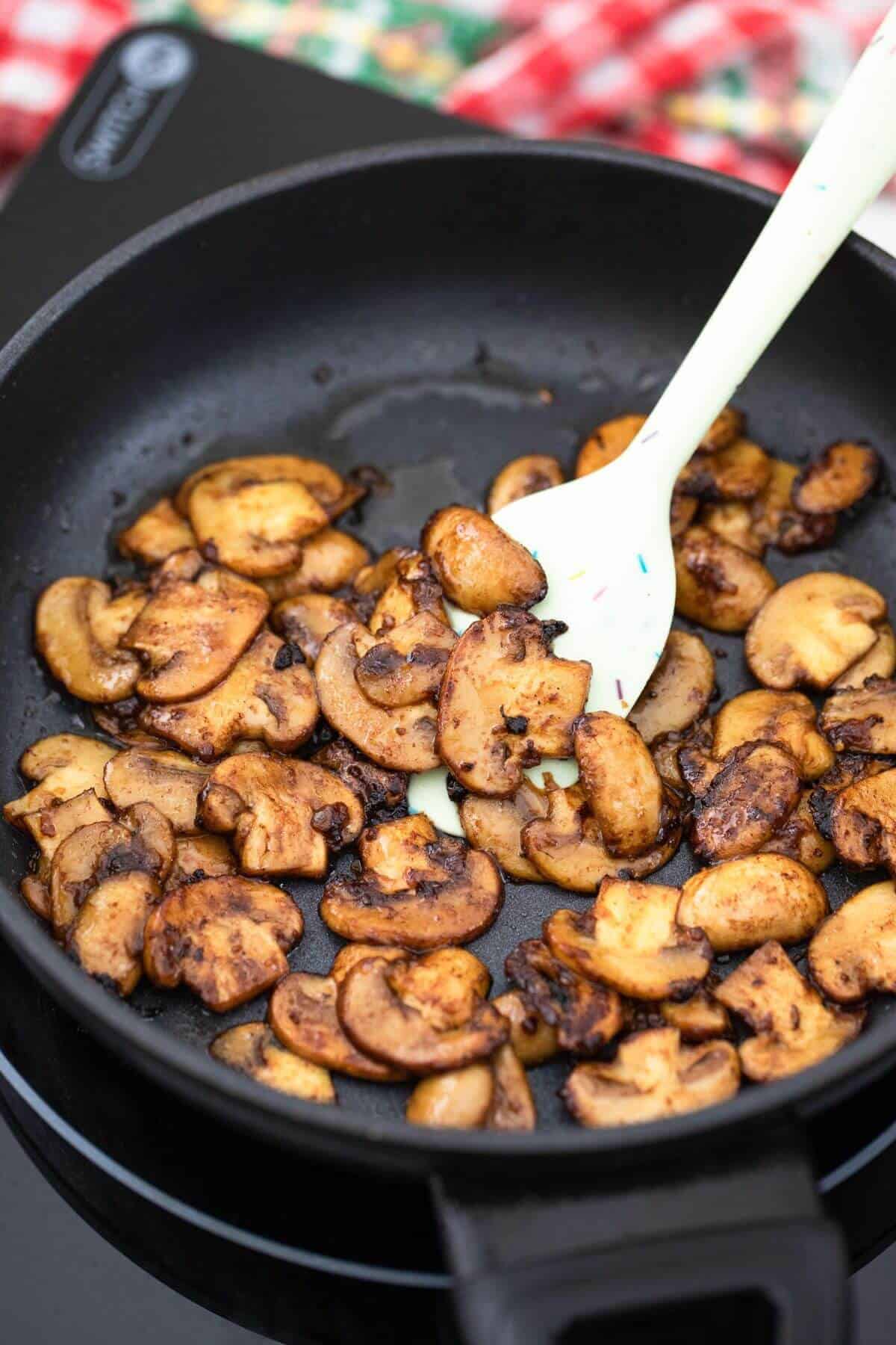 Fried mushrooms in a frying pan with a spoon.
