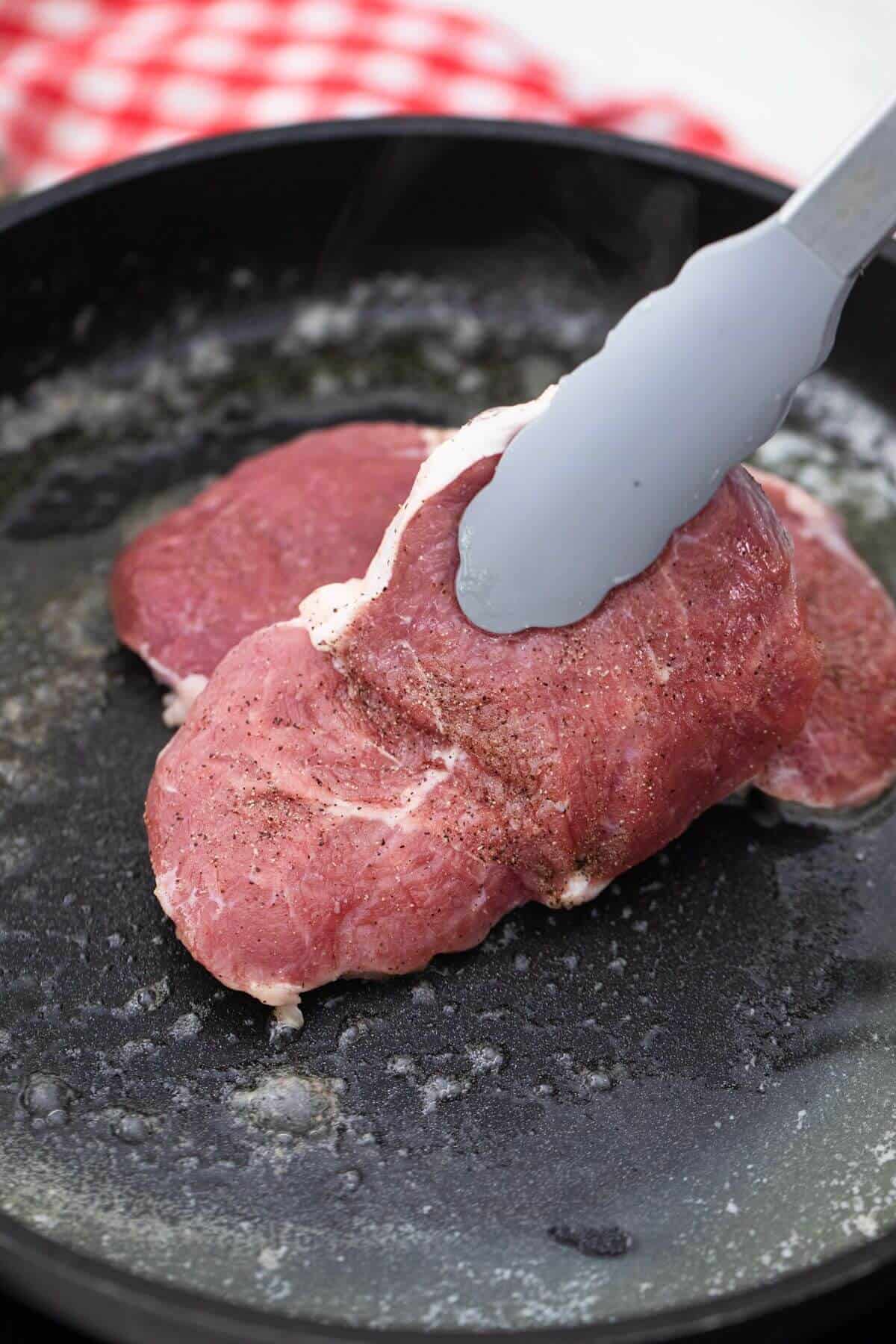 A piece of meat is being cooked in a frying pan.