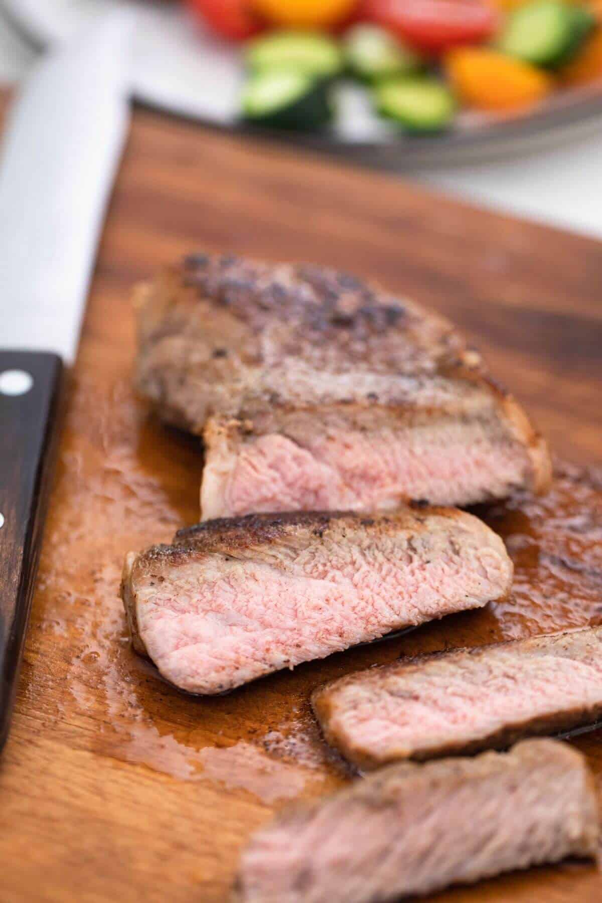 Steak on a cutting board with vegetables and a knife.