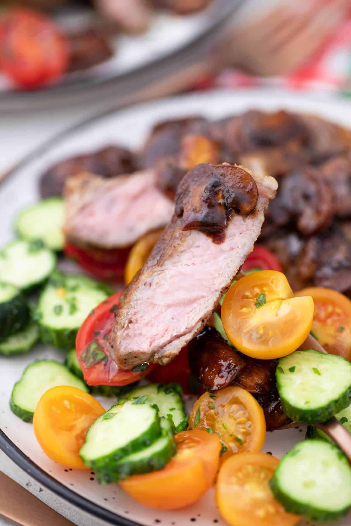 A plate with meat, tomatoes and cucumbers on it.