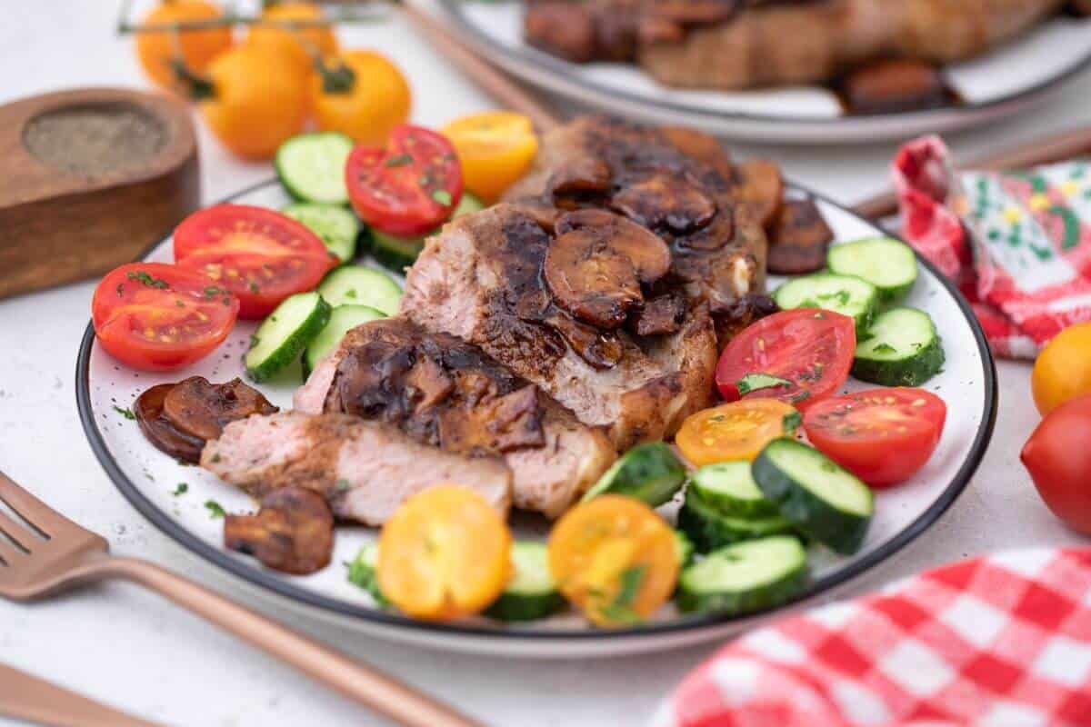 A plate with steak, mushrooms, tomatoes and cucumbers on it.