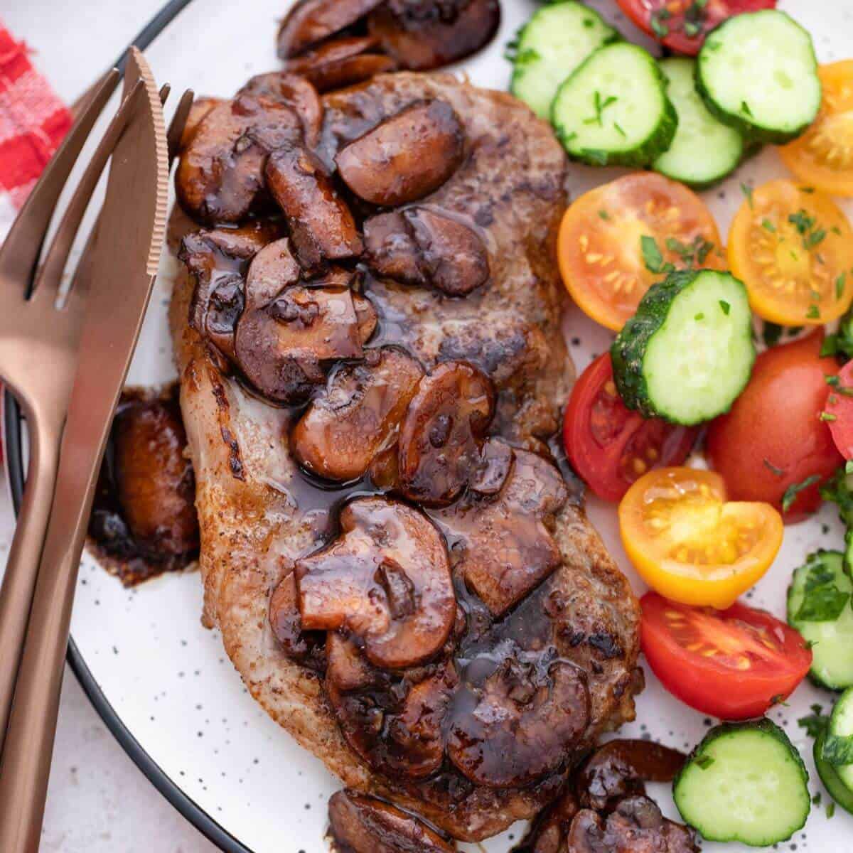 Steak and mushrooms with tomatoes on a plate.