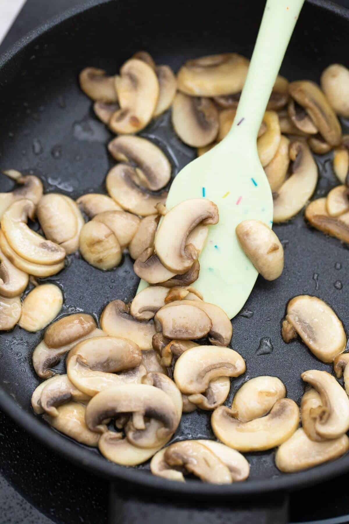 Mushrooms in a frying pan with a green spatula.