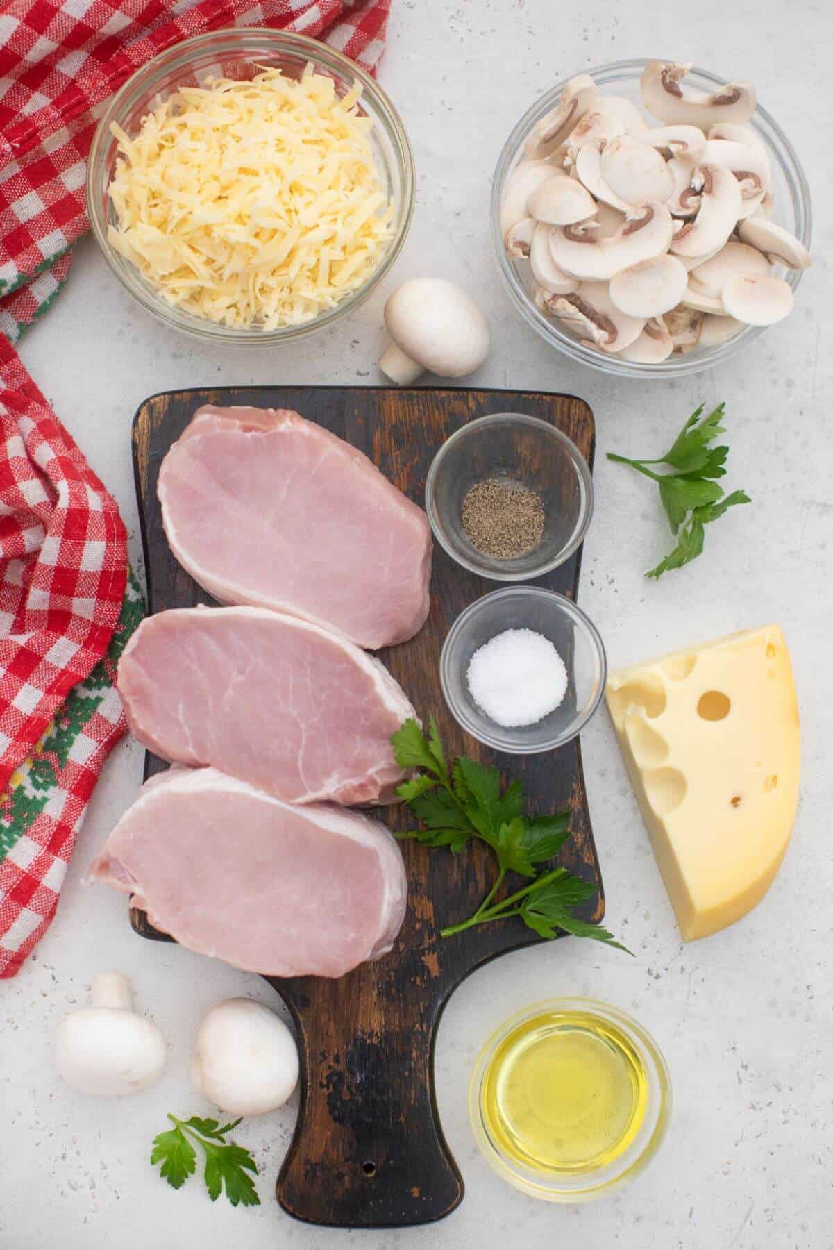 Boneless pork chops, cheese, mushrooms and other ingredients on a cutting board.