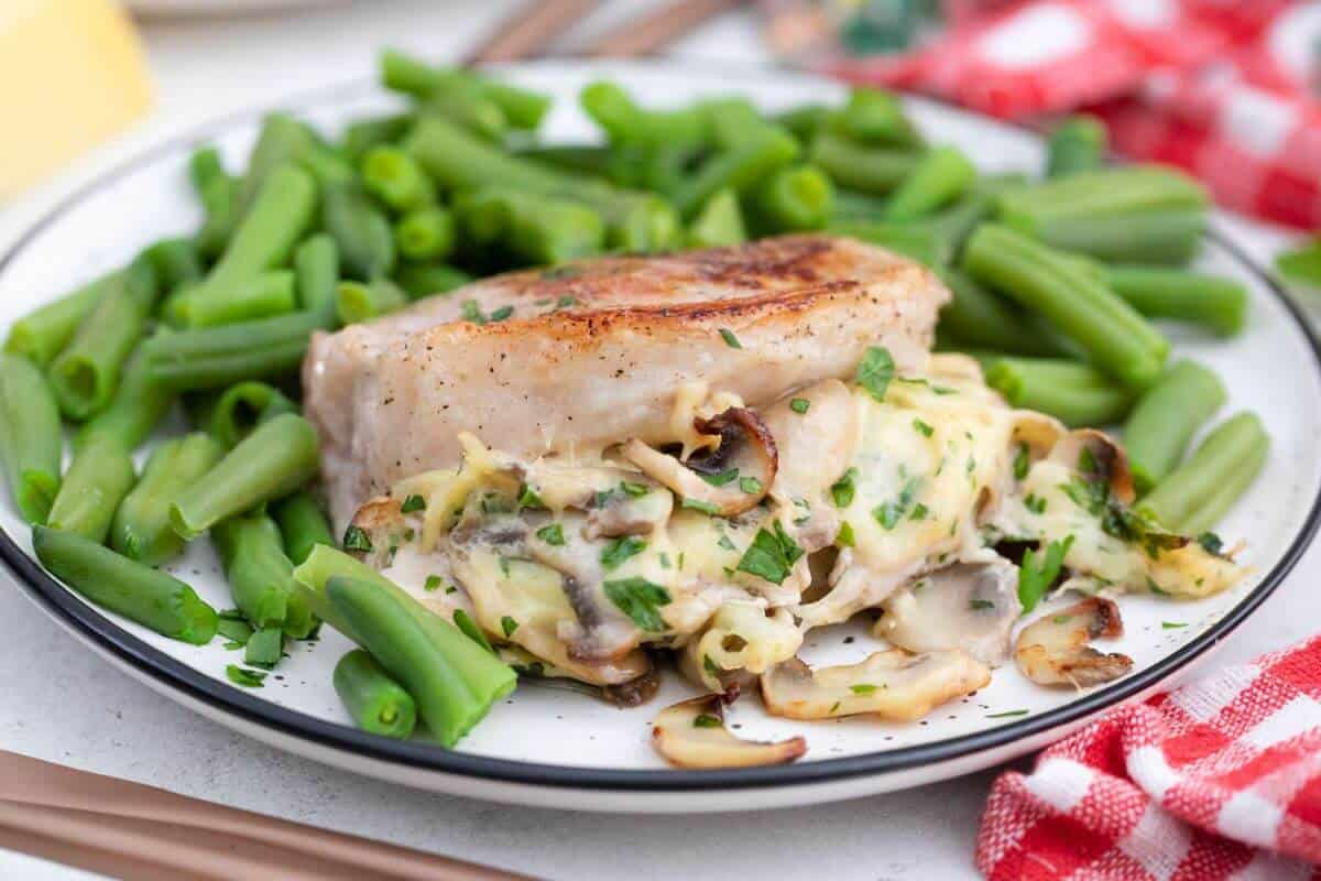 A plate of pork chops stuffed with mushrooms and cheese served with green beans.