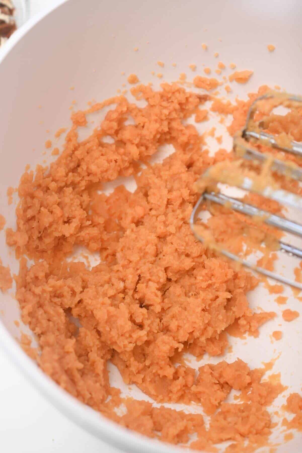 Beaten canned yams in a bowl with a whisk.