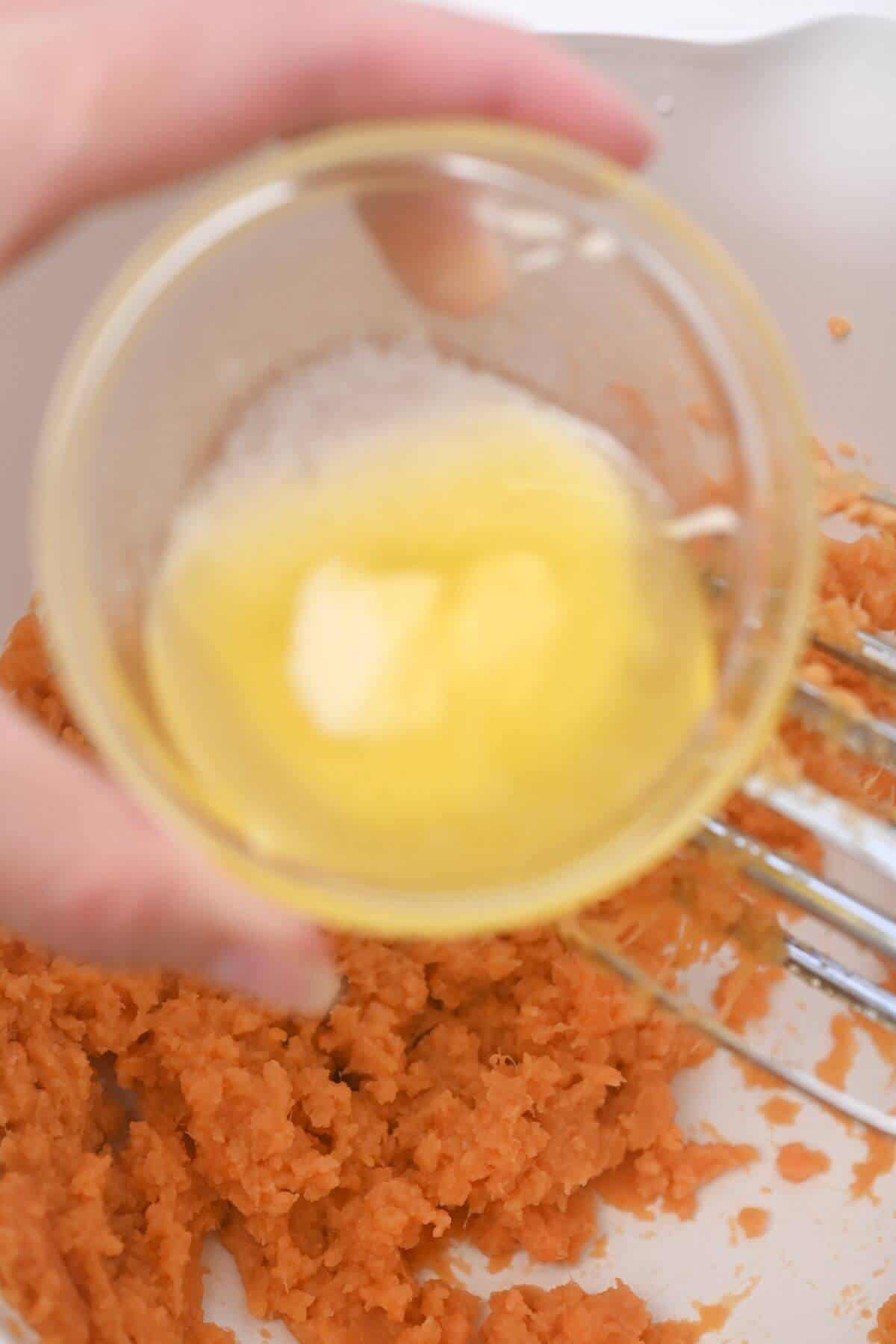 A person adding melted butter to ingredients in a bowl with canned yams.