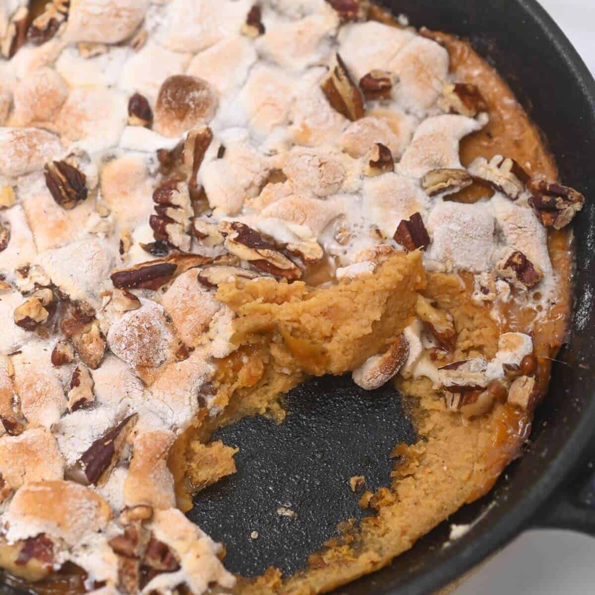 A delectable sweet potato casserole with canned yams topped with pecans and marshmallows, cooked to perfection in a skillet.