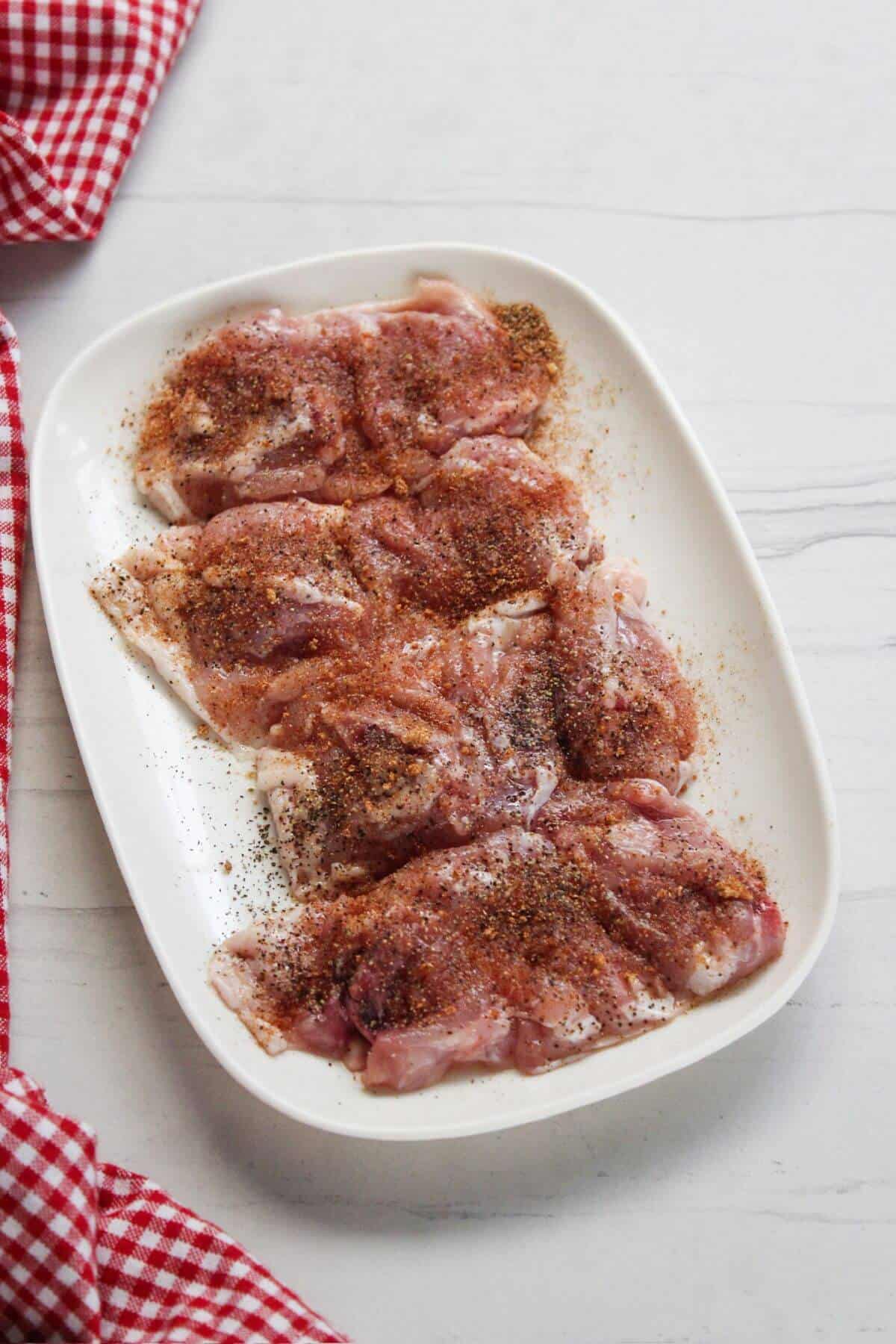 Seasoned chicken thighs on a white plate with a red and white checkered tablecloth.