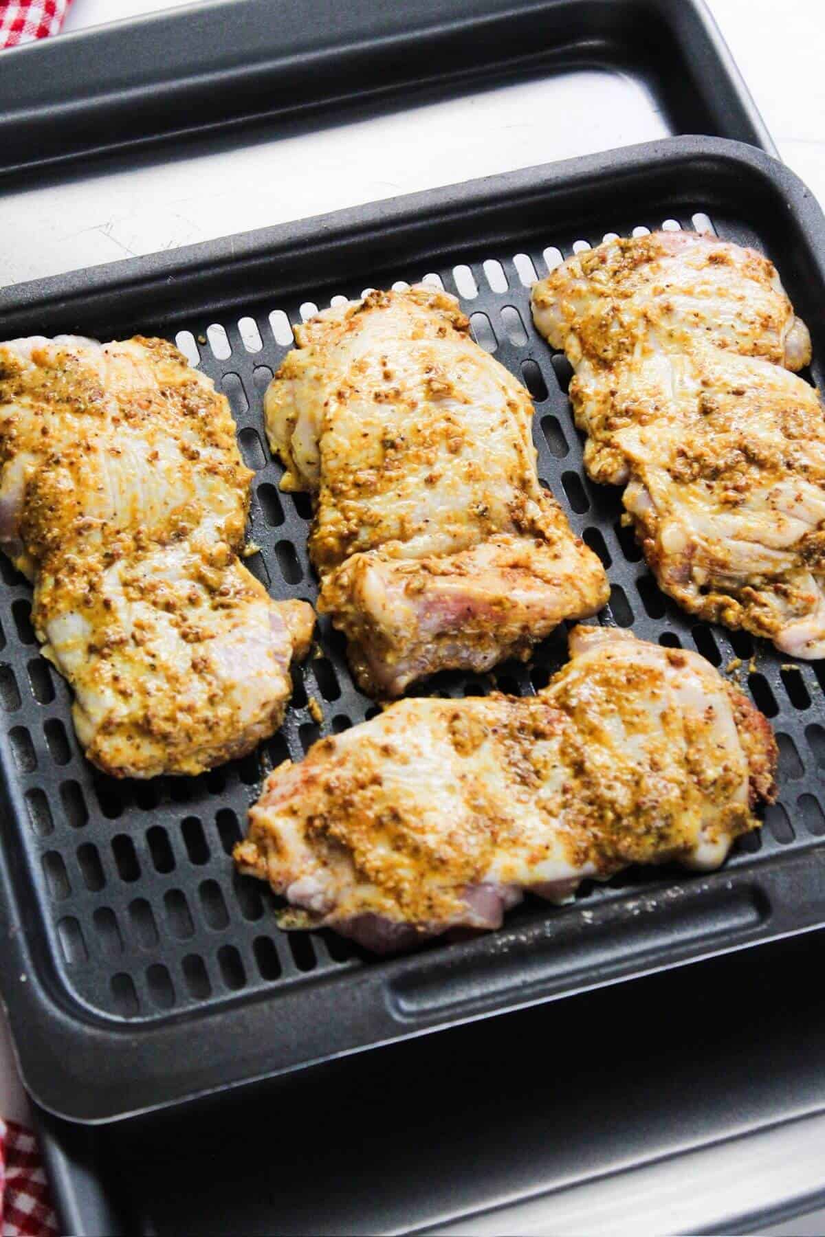 Chicken thighs on an air fryer pan on top of a checkered tablecloth.