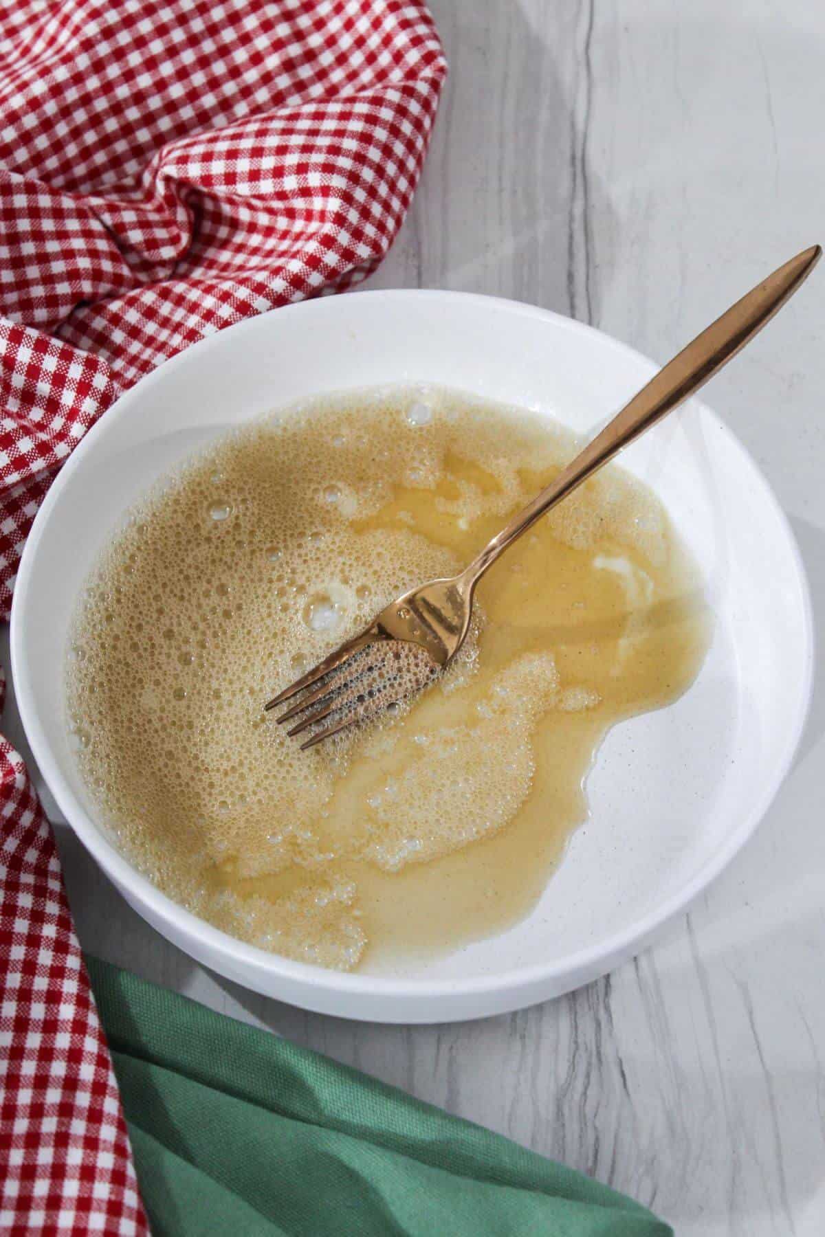 A white bowl with a fork on a red and white checkered napkin.