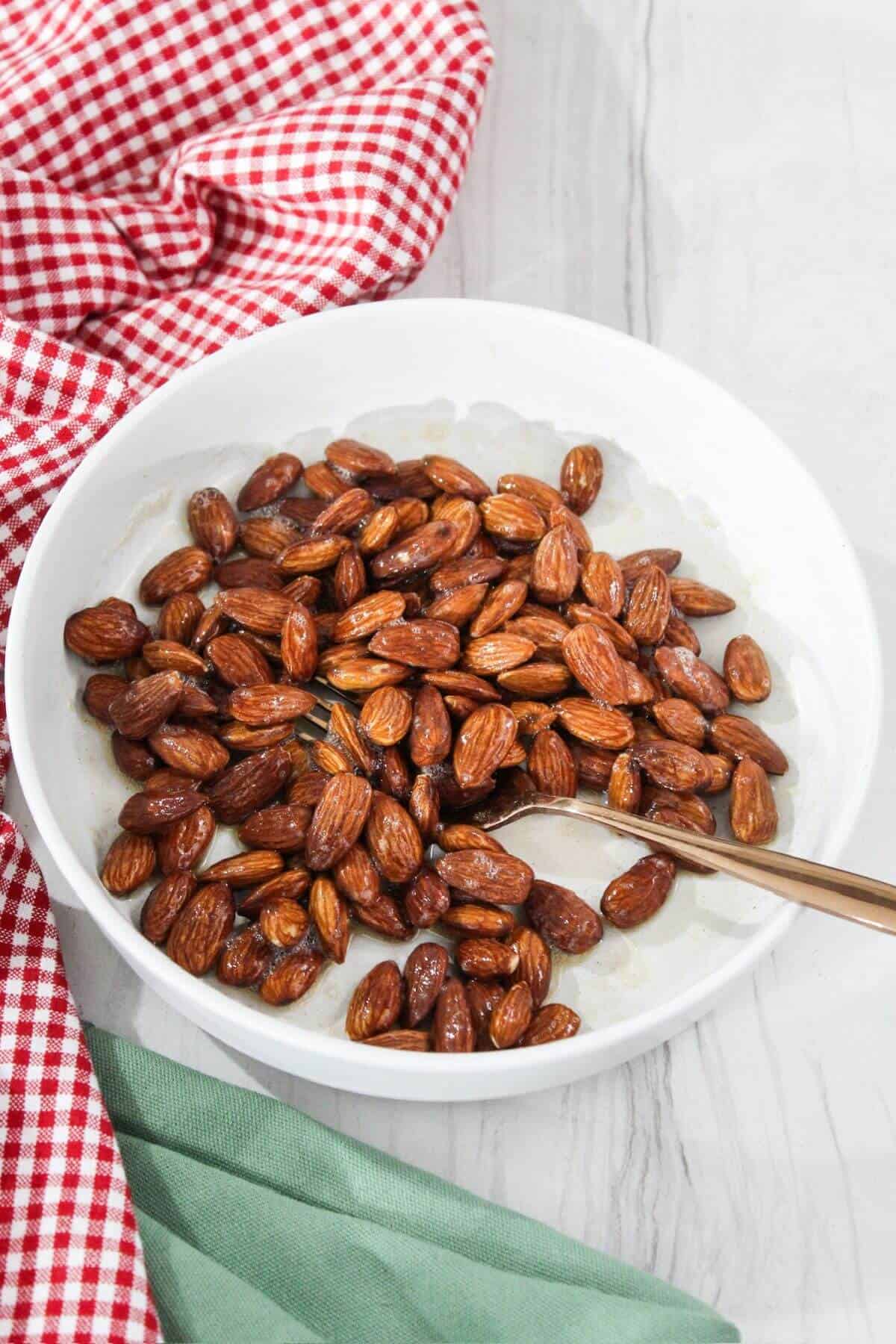 Egg coated almonds in a white bowl with a fork.