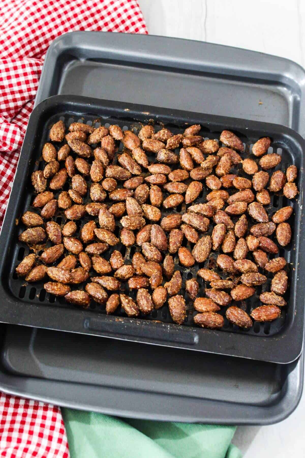 Candied almonds in an air fryer pan on a checkered napkin.