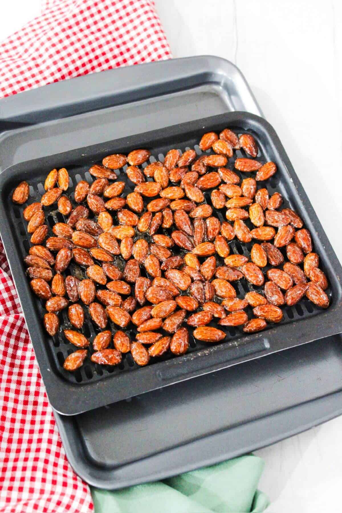 Candied almonds before cooking arranged in a baking pan on a red and white checkered tablecloth.