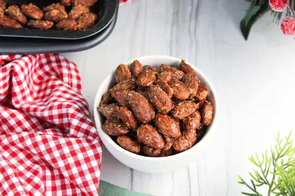 Candied almonds in a white bowl next to a red checkered tablecloth.