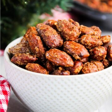 Candied almonds in a bowl next to a Christmas tree.