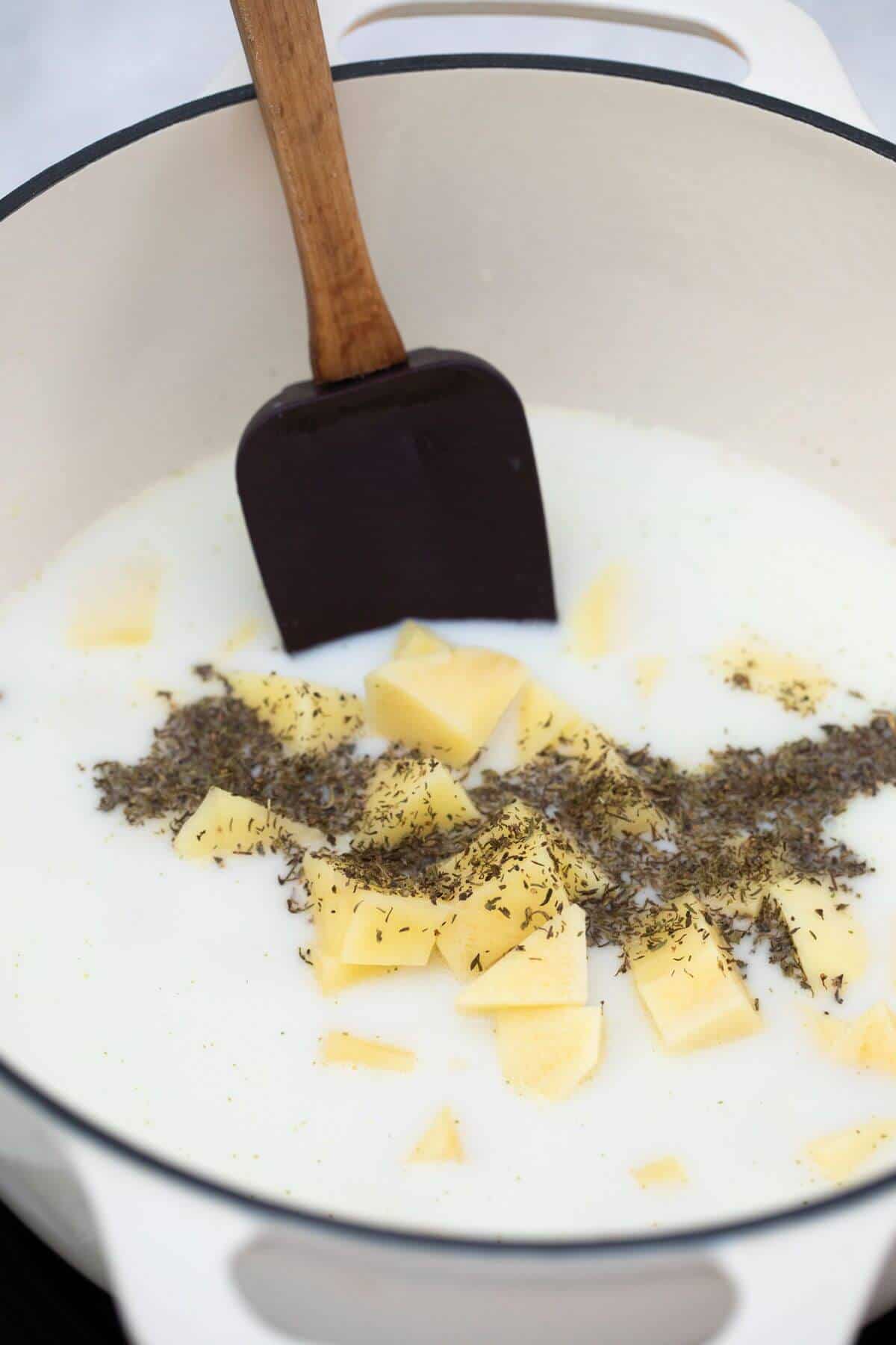 A pot of milk with spices and a wooden spoon.