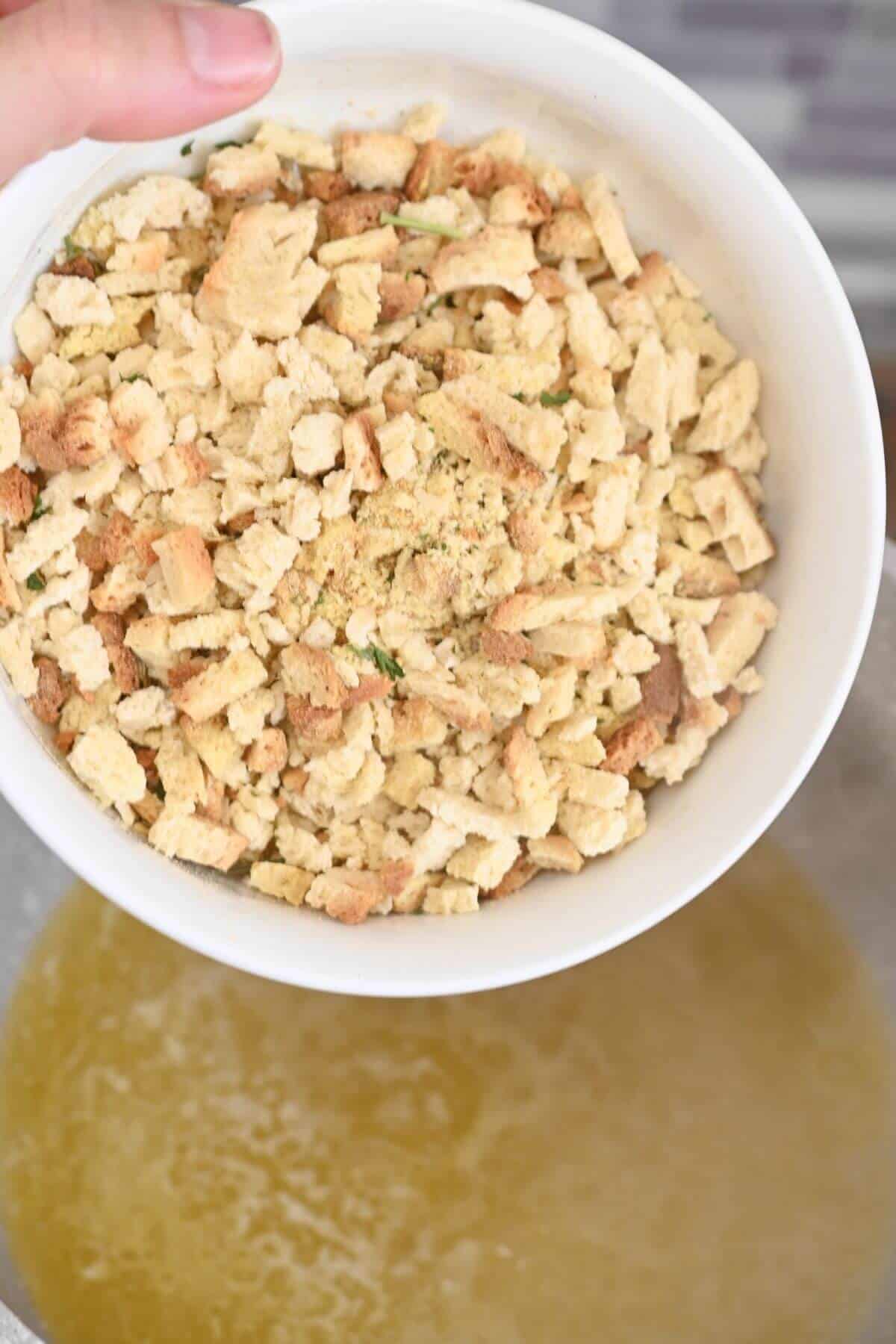 A person is holding a bowl of stuffing mix in a bowl.