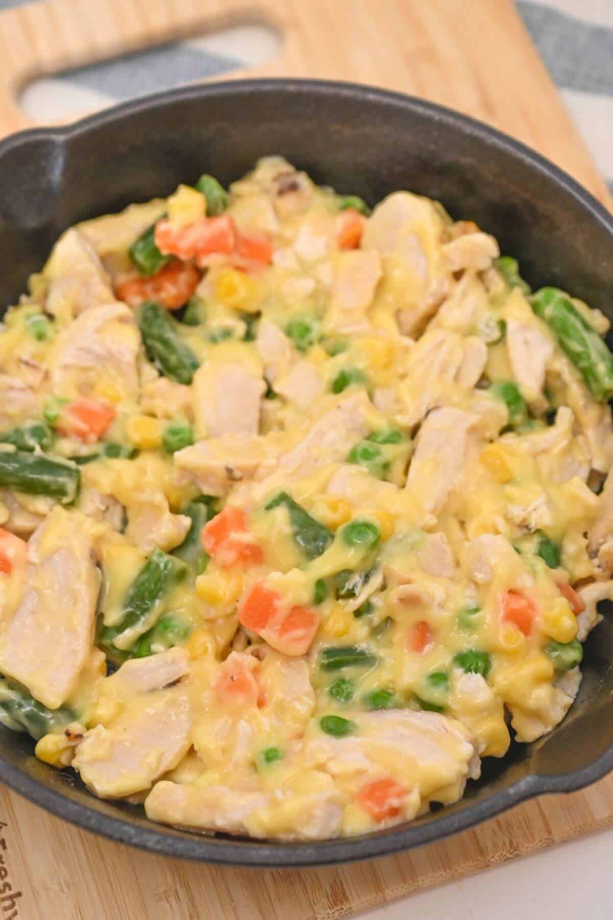 A skillet full of chicken and vegetables on a wooden cutting board.