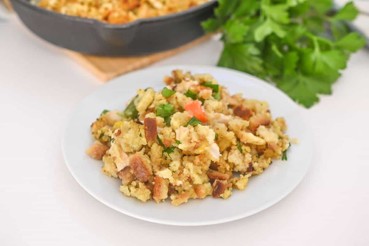 A plate of stuffing with chicken on a table next to a skillet.