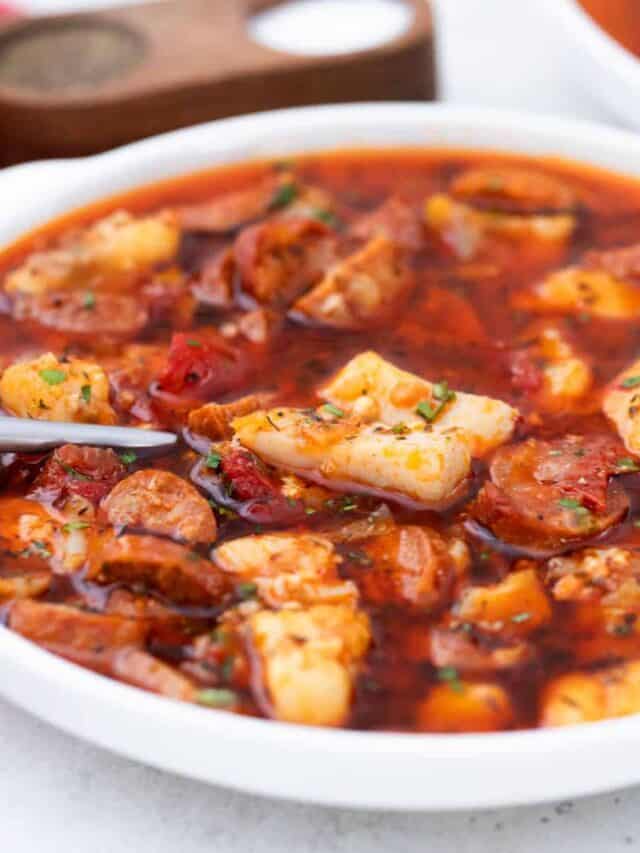A bowl of stew with sausage and tomatoes.