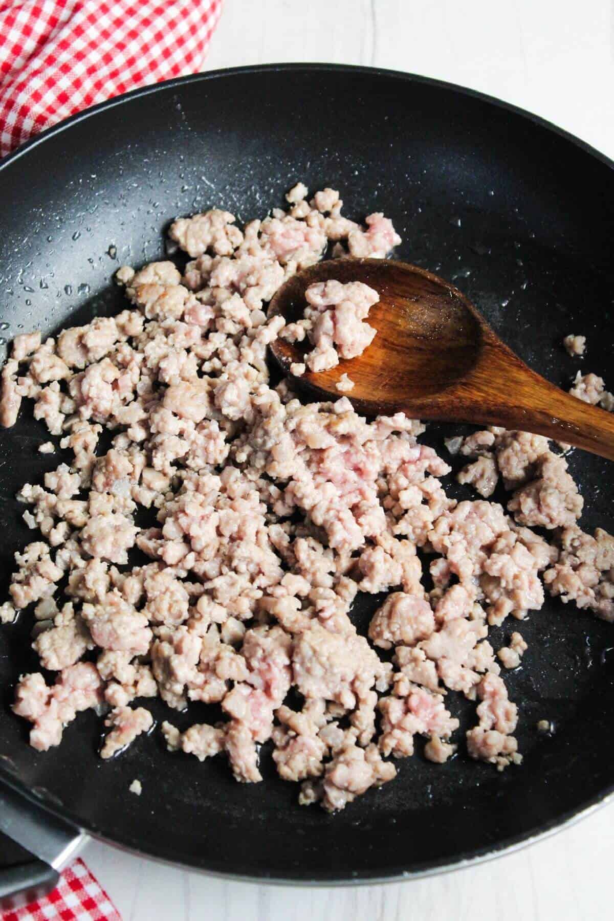Ground beef in a frying pan with a wooden spoon.